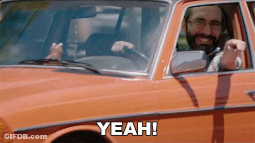 A Man With A Beard Is Driving An Orange Car And Says Yeah GIF