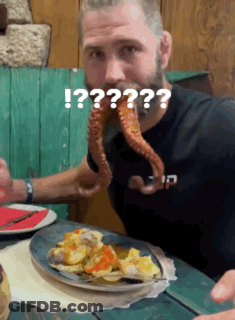 A Man With A Beard Is Eating A Plate Of Food With An Octopus Coming Out Of His Mouth .. GIF