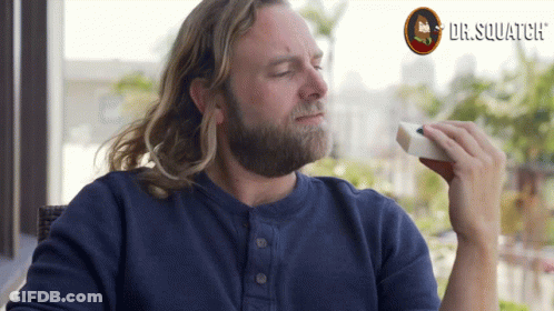 A Man With A Beard Is Eating A Sandwich With Dr. Squatch Written In The Background GIF
