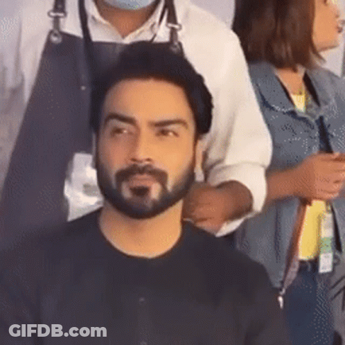 A Man With A Beard Is Getting His Hair Cut By A Hairdresser While A Woman Looks On . GIF