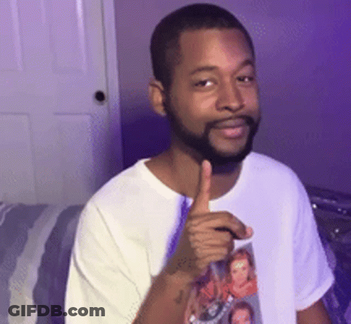 A Man With A Beard Is Giving A Thumbs Up While Wearing A White Shirt With A Picture On It . GIF