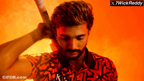 A Man With A Beard Is Holding A Bat In Front Of A Sign That Says 7Wick Reddy GIF