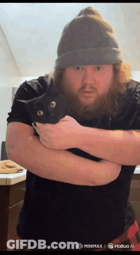 A Man With A Beard Is Holding A Black Cat In His Hands GIF