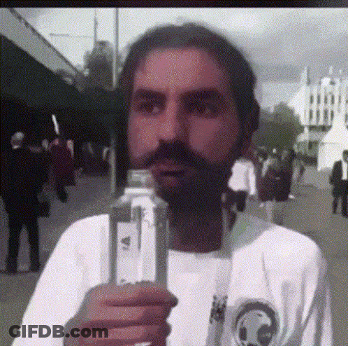 A Man With A Beard Is Holding A Bottle In His Hand GIF
