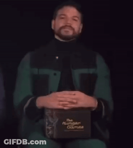 A Man With A Beard Is Holding A Box That Says The Hunger Games GIF
