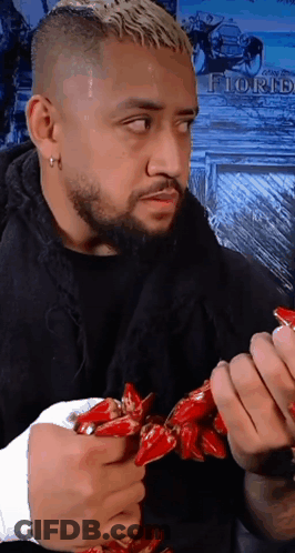 A Man With A Beard Is Holding A Bunch Of Red Peppers With The Word Florh On The Wall Behind Him GIF
