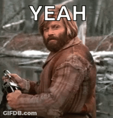 A Man With A Beard Is Holding A Camera And Says `` Yeah '' While Standing In The Woods . GIF