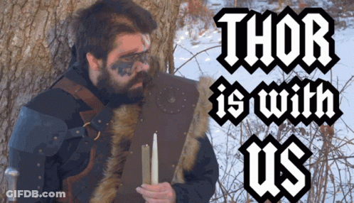 A Man With A Beard Is Holding A Candle In Front Of A Tree With The Words Thor Is With Us Above Him GIF