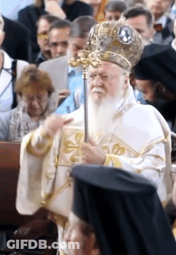 A Man With A Beard Is Holding A Cane In Front Of A Crowd Of People GIF