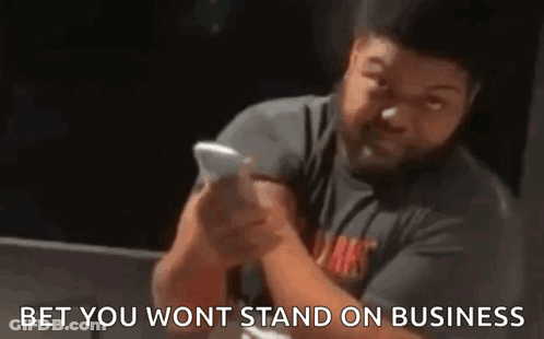 A Man With A Beard Is Holding A Cell Phone In His Hand . GIF