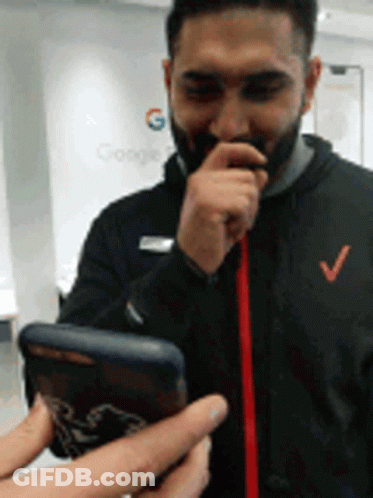 A Man With A Beard Is Holding A Cell Phone With A Google Logo In The Background GIF