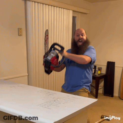 A Man With A Beard Is Holding A Chainsaw In Front Of A Window GIF