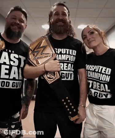 A Man With A Beard Is Holding A Championship Belt Next To Two Other People GIF