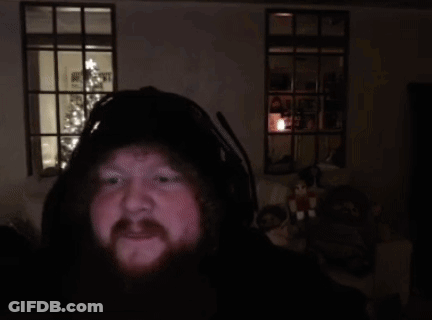 A Man With A Beard Is Holding A Donut In Front Of A Christmas Tree In A Dark Room . GIF