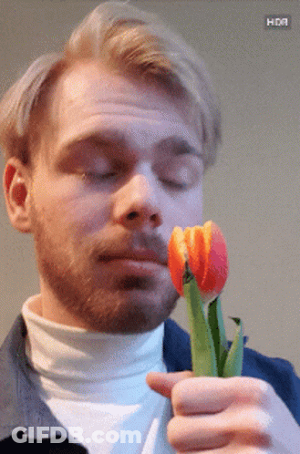 A Man With A Beard Is Holding A Flower In His Hand With A Hdr Button Below It GIF