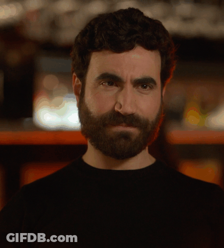 A Man With A Beard Is Holding A Glass In Front Of His Face GIF