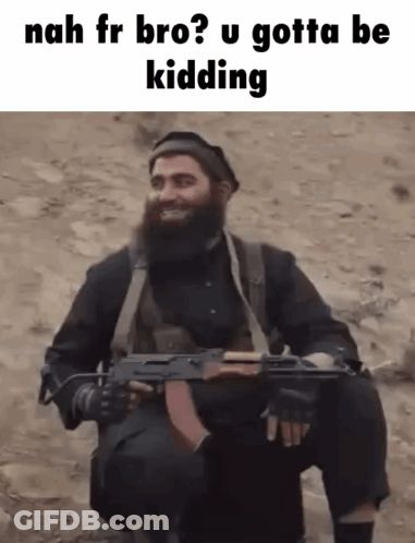 A Man With A Beard Is Holding A Gun And Smiling While Sitting In The Dirt . GIF