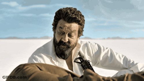 A Man With A Beard Is Holding A Gun In A Field GIF