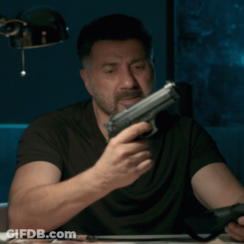 A Man With A Beard Is Holding A Gun In His Right Hand GIF