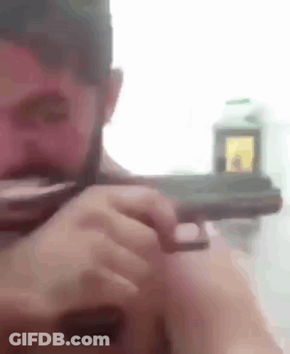 A Man With A Beard Is Holding A Gun In His Right Hand . GIF