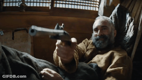 A Man With A Beard Is Holding A Gun GIF