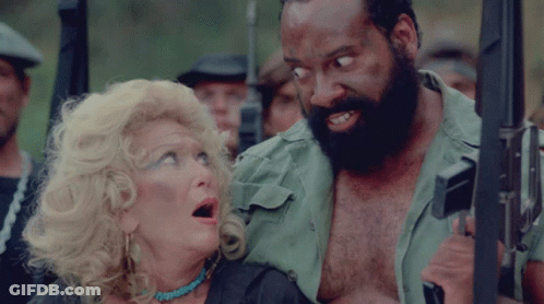 A Man With A Beard Is Holding A Gun Next To A Woman GIF