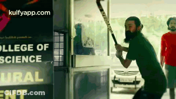 A Man With A Beard Is Holding A Hockey Stick In Front Of A College Of Science Sign GIF