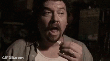 A Man With A Beard Is Holding A Key To His Chest In A Dark Room . GIF