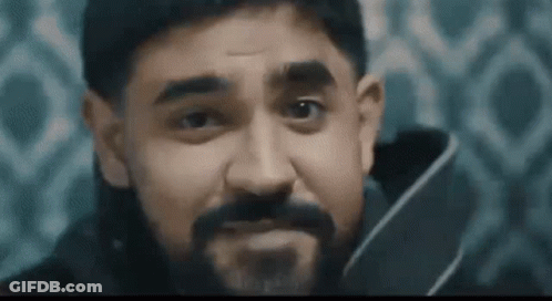 A Man With A Beard Is Holding A Knife In His Hand And Making A Face . GIF