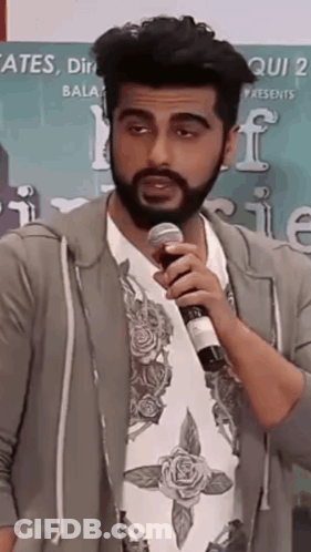 A Man With A Beard Is Holding A Microphone And Talking Into It . GIF