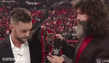 A Man With A Beard Is Holding A Microphone And Talking To Another Man In A Suit . GIF
