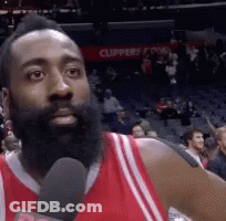 A Man With A Beard Is Holding A Microphone In Front Of A Crowd . GIF