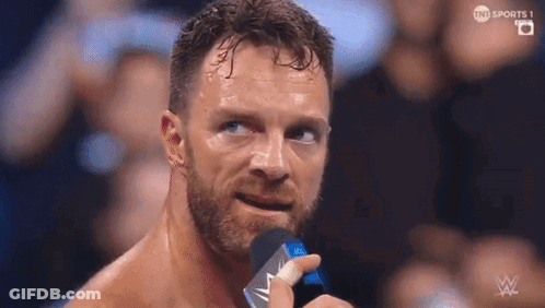 A Man With A Beard Is Holding A Microphone In Front Of His Face . GIF