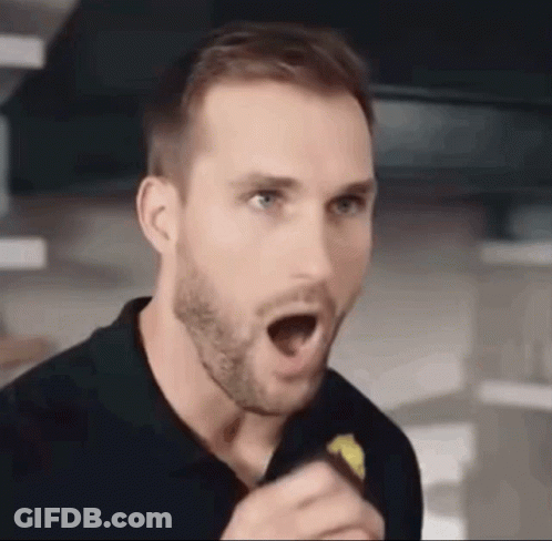 A Man With A Beard Is Holding A Piece Of Food In His Hand And Making A Surprised Face . GIF