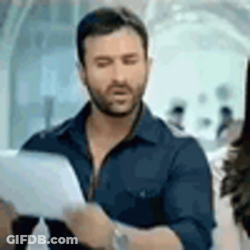 A Man With A Beard Is Holding A Piece Of Paper And Looking At It . GIF