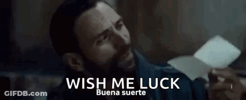 A Man With A Beard Is Holding A Piece Of Paper With The Words `` Wish Me Luck '' Written On It . GIF
