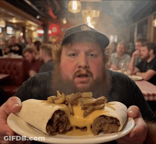 A Man With A Beard Is Holding A Plate Of Food With A Gk Hat On GIF