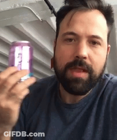 A Man With A Beard Is Holding A Purple Can Of Soda With The Letter T On It GIF