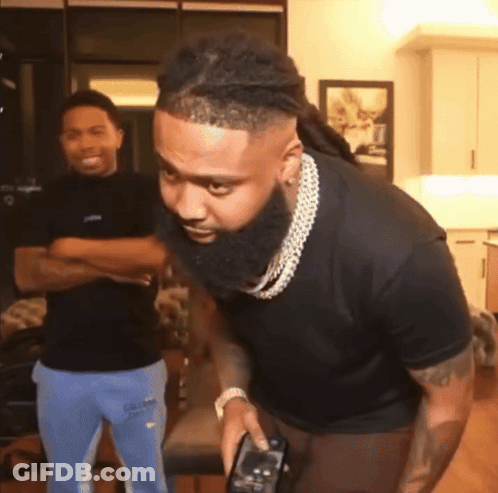 A Man With A Beard Is Holding A Remote Control In His Hand GIF