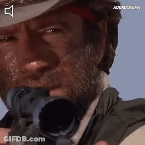 A Man With A Beard Is Holding A Sniper Rifle In Front Of His Face . GIF
