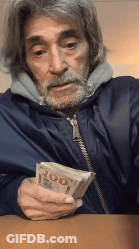 A Man With A Beard Is Holding A Stack Of 100 Dollar Bills GIF