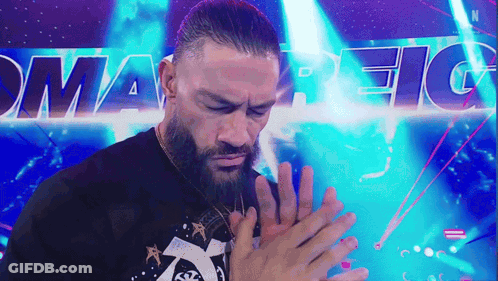 A Man With A Beard Is Holding His Hands Together In Front Of A Sign That Says Smart Fight . GIF