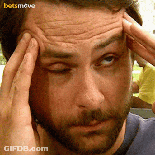 A Man With A Beard Is Holding His Head While Looking At The Camera . GIF