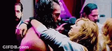 A Man With A Beard Is Hugging A Woman In A Crowded Room . GIF