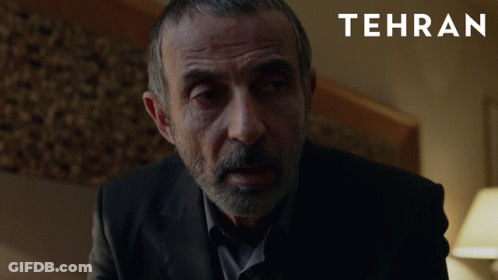 A Man With A Beard Is In A Dark Room With Tehran Written On The Bottom GIF