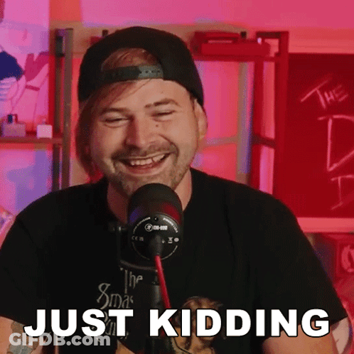 A Man With A Beard Is Laughing In Front Of A Microphone And The Words Just Kidding Are Visible GIF