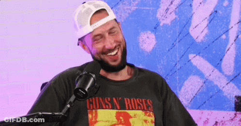 A Man With A Beard Is Laughing In Front Of A Microphone Wearing A Guns N ' Roses Shirt . GIF