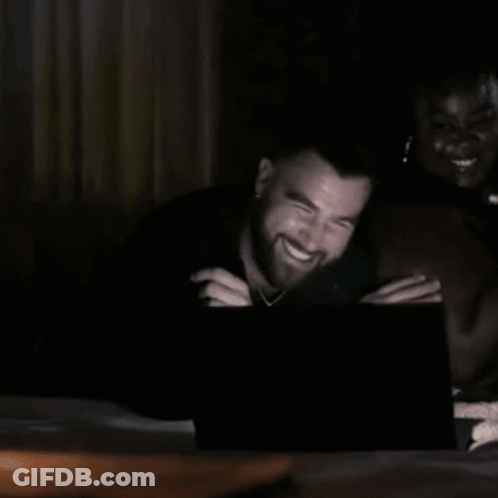 A Man With A Beard Is Laughing While Looking At A Laptop Screen . GIF