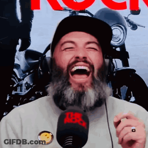 A Man With A Beard Is Laughing While Wearing Headphones And A Hat With The Word Rock On It GIF