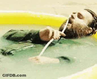 A Man With A Beard Is Laying In A Pool Drinking Water Through A Straw GIF